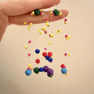 Close-up of vibrant multi-color beaded tassel earrings held by hand on a warm background