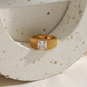 Gold wide band ring with square white crystal on an artistic terrazzo stone base