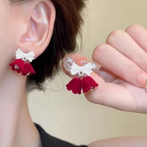 Detail of red velvet flower earrings with a white ribbon bow design on a model's ear