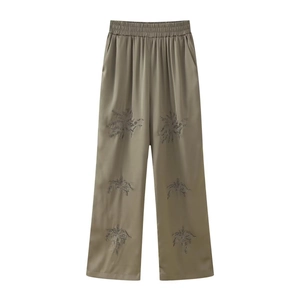 Detail of olive satin wide-leg trousers featuring intricate floral beadwork and embroidery