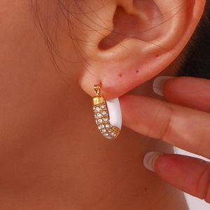Detailed view of U-shaped gold plated earrings with white enamel and pavé zircons on ear