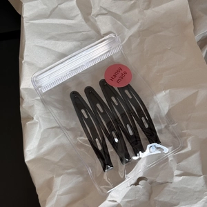 Detail of four black metal teardrop hair clips in a transparent minimalist packaging bag