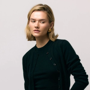 Close-up of elegant gold textured oval stud earrings on a model wearing green knitwear