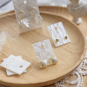 Elegant gold earrings on marble display cards presented in a round wooden tray