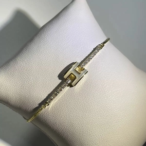 Detailed shot of gold-plated T-shaped bracelet with H logo and pavé-set cubic zirconia