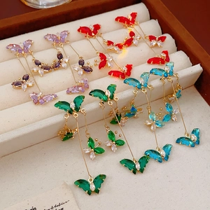 Détail de boucles d'oreilles papillon à pompons colorés avec cristaux violets, rouges et bleus