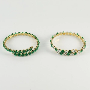 Detail of two gold-plated spiral bangles with inlaid green and white cubic zirconia