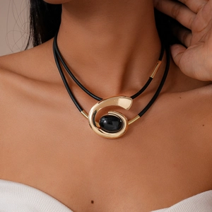 Close-up of double-layer black cord necklace with a gold spiral pendant and black gemstone