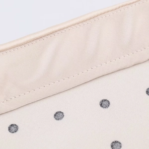 Close-up of beige satin fabric with black polka dots and high-quality stitching detail