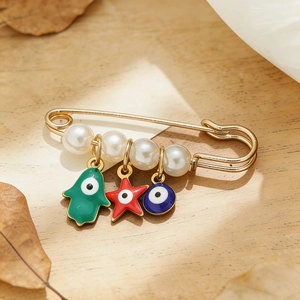 Détail de la broche dorée avec perles blanches et pendentifs en émail mauvais oeil