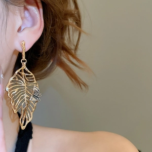 Close-up of golden hollow leaf earrings with small butterfly accent on a model