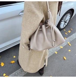 Detail of a beige drawstring bucket bag with litchi grain leather and silver metal charm