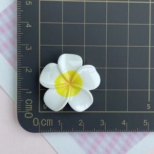Macro shot of a 3cm white and yellow resin frangipani flower on a black grid mat