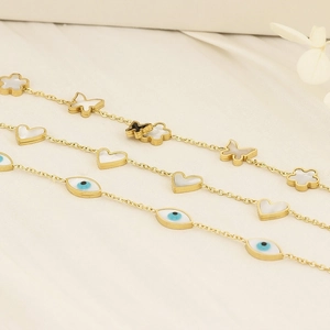 Detail of gold titanium steel bracelets with shell hearts, butterflies and evil eye charms
