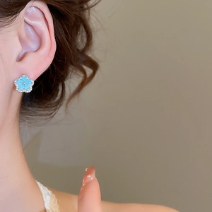 Close-up of light blue enamel flower earring with rhinestones on a female ear
