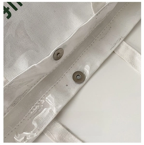 Detail of hardware magnetic buckle closure on a white canvas and transparent PVC tote bag