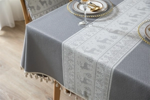 Detail of grey jacquard tablecloth featuring white reindeer patterns and decorative fringe