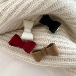 Détail de barrettes à nœuds en velours de quatre couleurs sur un pull en maille blanche