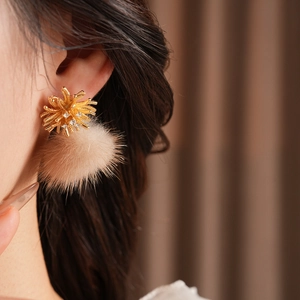 Close-up of model wearing gold zircon firework stud earrings with beige pompom drop