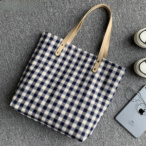 Detail der blau karierten Canvas-Tasche mit Ledergriffen und goldenen Nietenakzenten