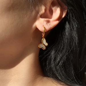 Detailed close-up of 18K gold butterfly earring with white shell inlay worn by a model