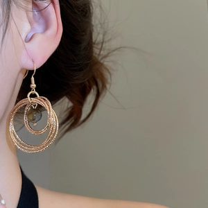 Close-up of model wearing gold layered circular hoop earrings with tiger eye stone