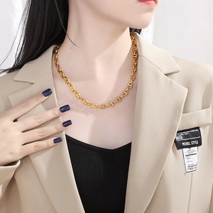 Golden stainless steel pig nose chain necklace worn by a model in a beige blazer