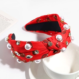 Détail d'un bandeau noué en tissu rouge orné de perles et de strass brillants