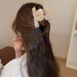 Detail view of large beige plush hair claw clip worn in hair showing fluffy texture