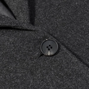 Macro detail of charcoal grey wool fabric texture and black button on a mid-length coat