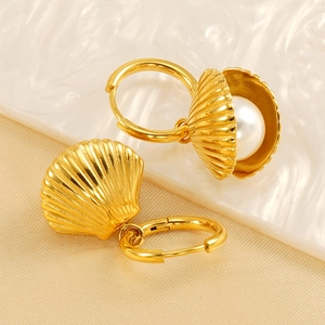 Elegant gold shell earrings with white pearl detail on textured minimalist background