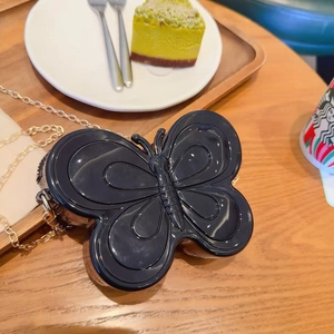 Vue détaillée du sac papillon noir avec chaîne dorée sur une table de café