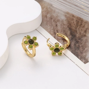 Detail of gold flower earrings with green crystals on white geometric stand