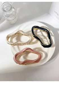 Set of three large wavy hair claws in cream, black and pink on a white ceramic tray