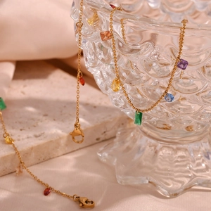 Detail of 18K gold-plated necklace with colorful geometric zircon stones on glass bowl