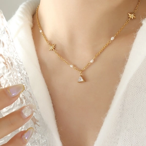 Elegant gold titanium necklace with star charms and pearl on white sweater