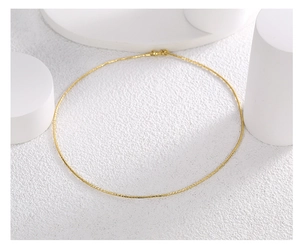 Minimalist gold collar necklace displayed on a white textured surface with geometric props