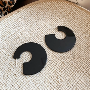 Detail shot of black acrylic geometric C-shape stud earrings on a ceramic tray