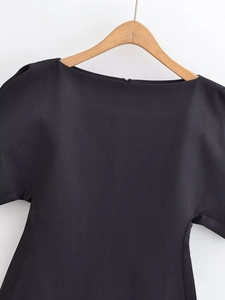 Détail d'un haut noir élégant avec encolure bateau et tissu lisse sur un cintre