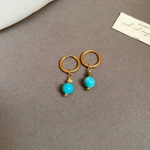 Close-up of gold hoop earrings with blue turquoise beads on a minimalist grey background