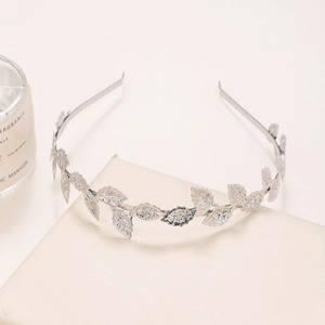 Detailed view of leaf-shaped silver metal headband on a beige textured cushion