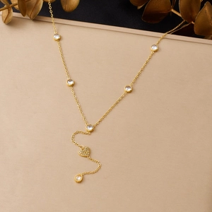 Détail du collier en Y doré avec pendentif cœur, zircons et chaîne à pompon élégante