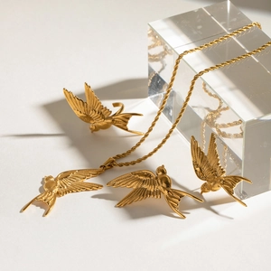 Detailed close-up of golden bird jewelry set with engraved feather textures and rope chain