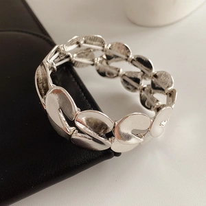 Close-up of a wide silver elastic bracelet with a textured wave pattern on dark leather