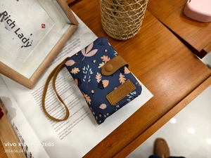 Detail of navy canvas wallet with floral pattern and brown leather buckle on a desk