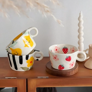 Detailed view of hand-painted ceramic mugs with fruit and floral patterns in irregular shapes