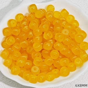 Detailed view of 6x8mm yellow translucent resin barrel beads in a white ceramic dish