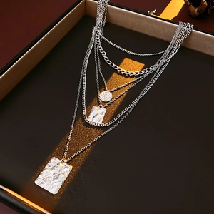 Detailed macro view of layered silver necklace featuring hammered square and round pendants