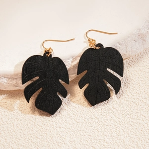 Detail of black monstera leaf wooden earrings with gold hooks on a textured pedestal