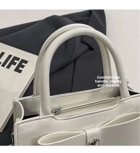 Detail of white bow handbag with heart buckle and silver zipper on a textured leather base